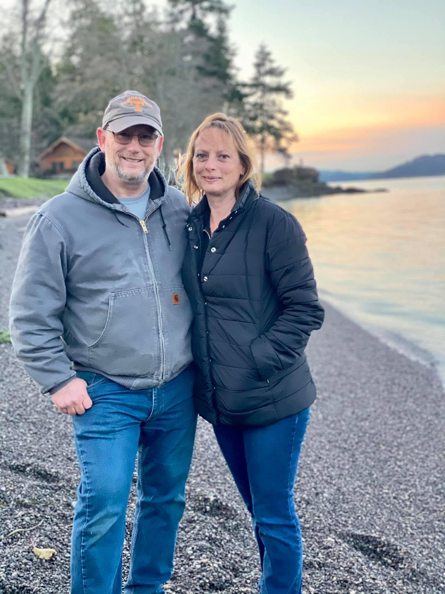 Tami and Ray standing together on a pebble beach at sunset