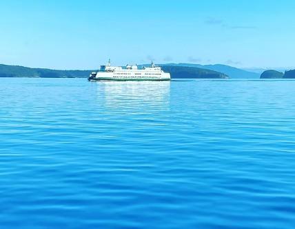 A Washington State Ferry crossing calm blue water between forested islands